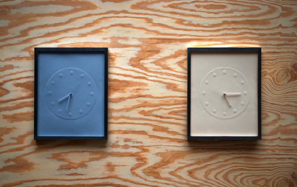 A clock made of embossed paper and presented in a custom frame.