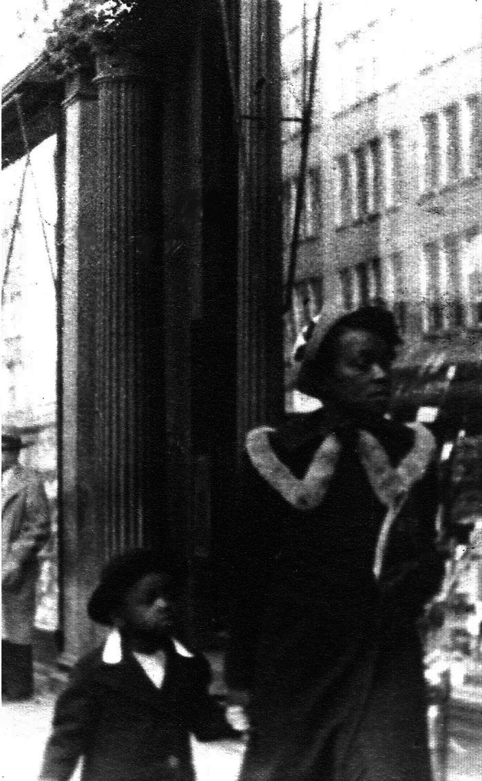 Black and white photograph of a small girl holding her mother's hand as they walk down the street