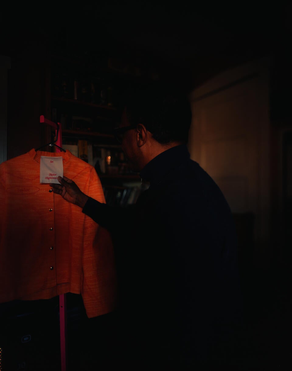 Man in the right-hand side of the frame looking over his shoulder at an orange jacket hanging from a clothing rack.