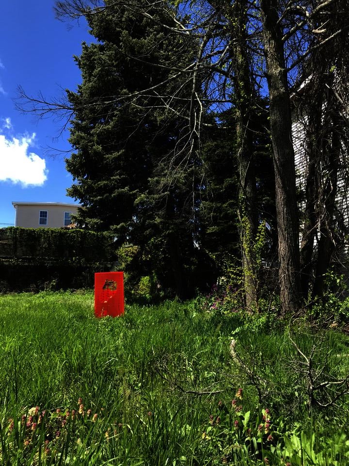 An orange plastic box with cut-outs sits in a grassy yard beneath trees.