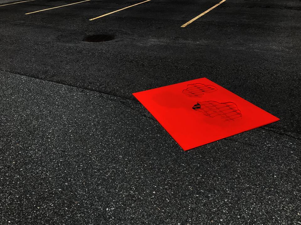 A flat orange plastic rectangle with cut-outs lays on the asphalt of an empty parking lot.
