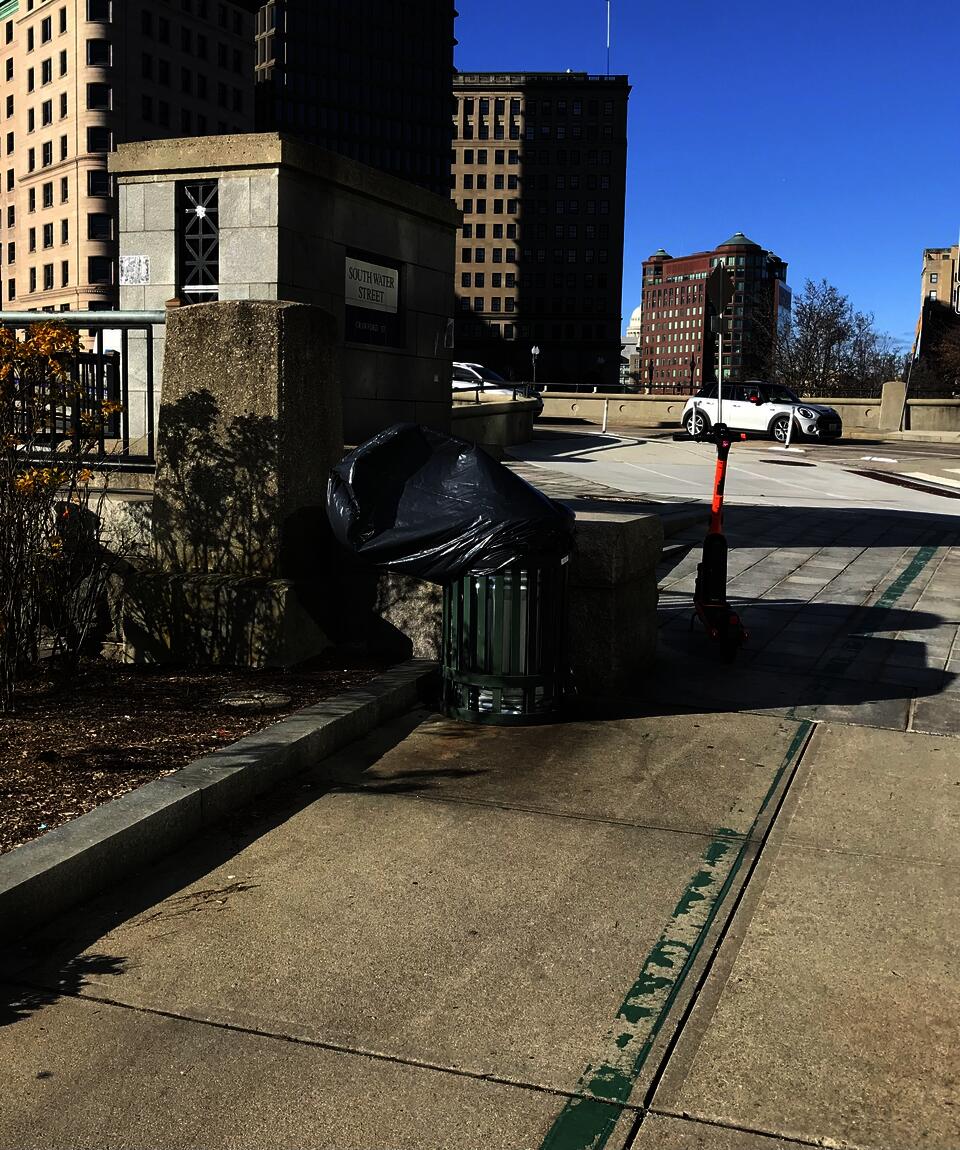 A trash can along the Providence River with the bag blowing around above the can in the wind.