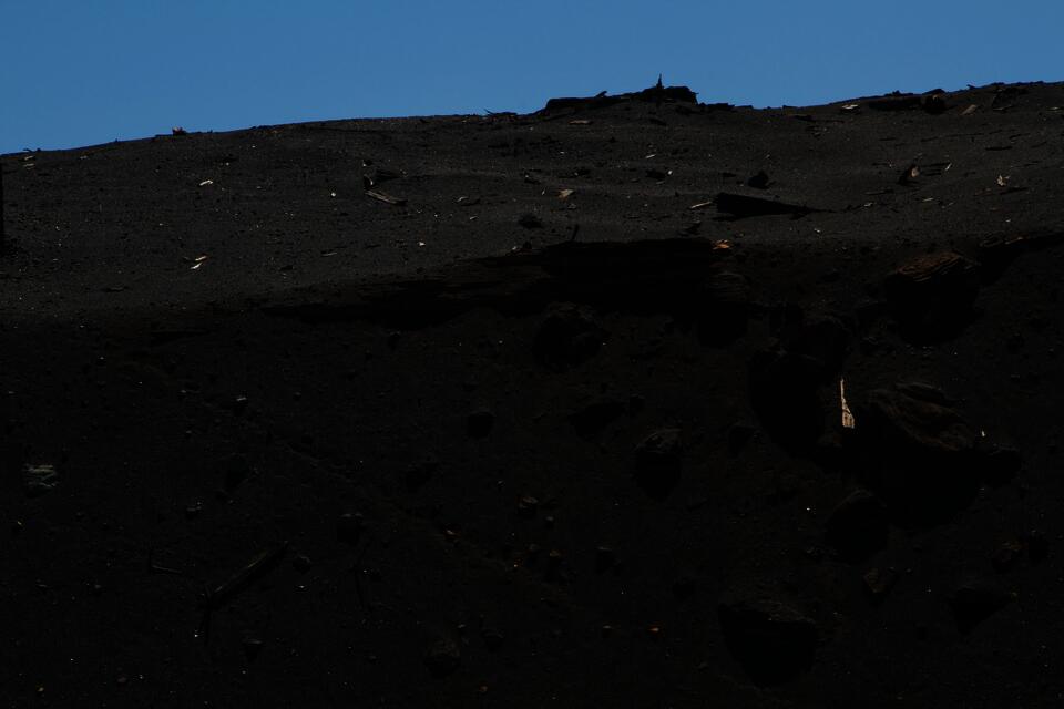 A spectral photograph of copper sulfide ore hovers in front of a greyscale background of glitched archival scans. The scans are nearly illegible but depict mining technology, the lower half of a Marcus Daly statue, and text from a Butte visitor's guide. 