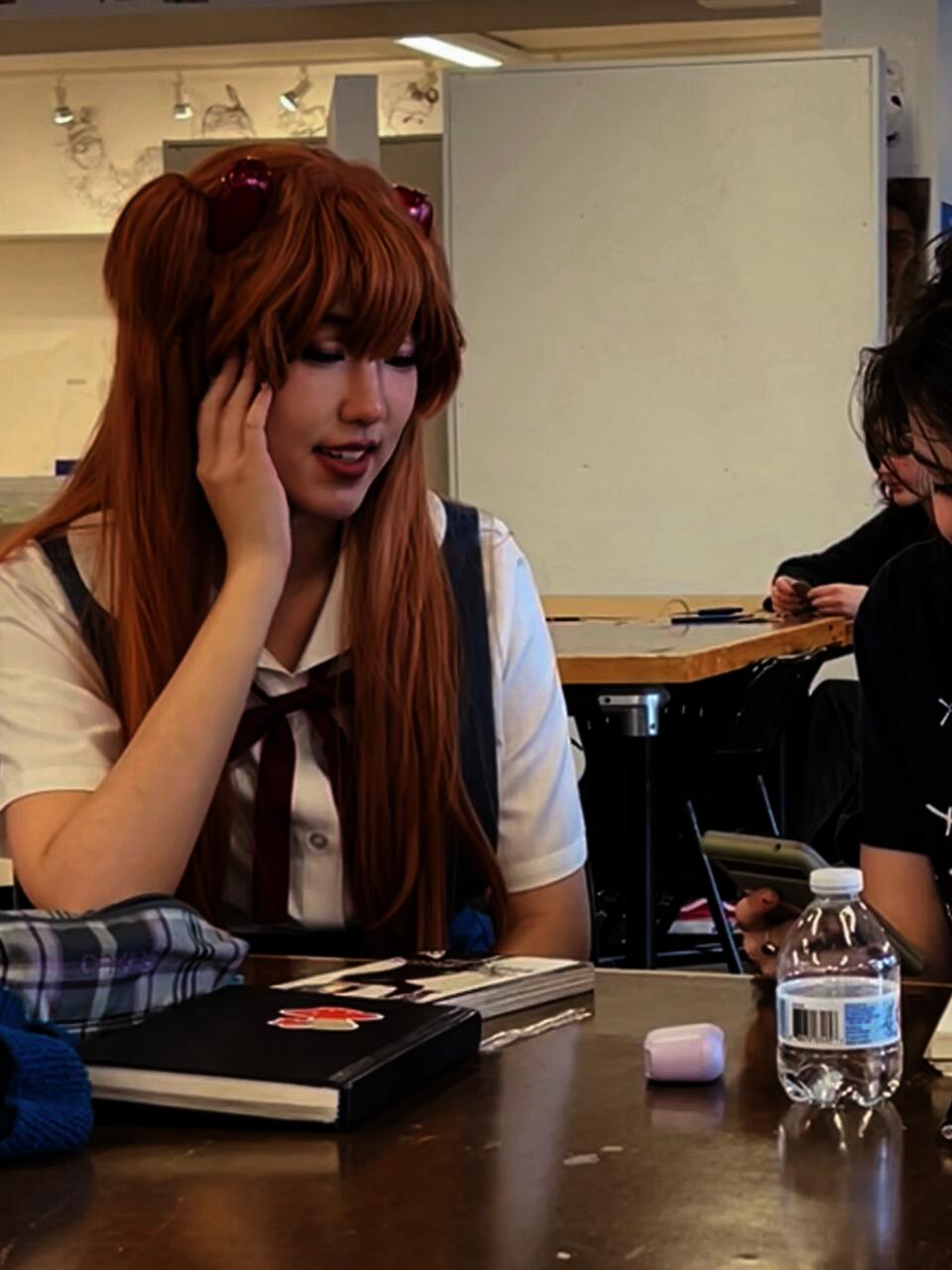 The author dressed as Asuka Langley Soryu, a female fictional character from the Japanese franchise Neon Genesis Evangelion, discussing development plans with a student.