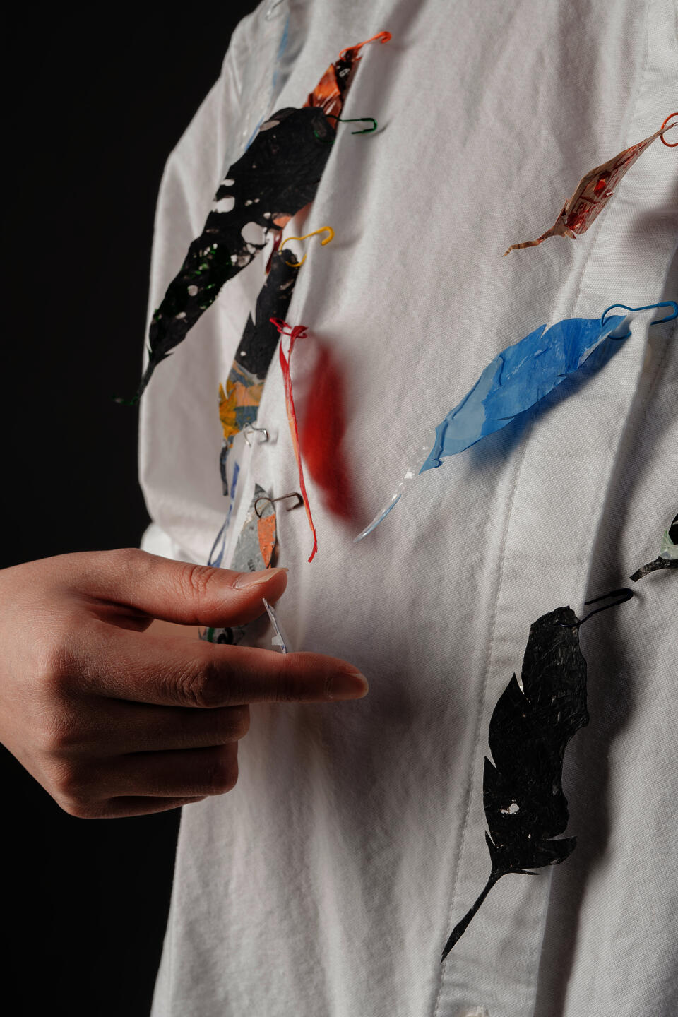 A photo of a model wearing feather brooches, with a hand appearing in the photo.