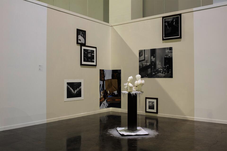 Installation of unframed and framed photographs in a gallery corner, with a wax sculpture front.