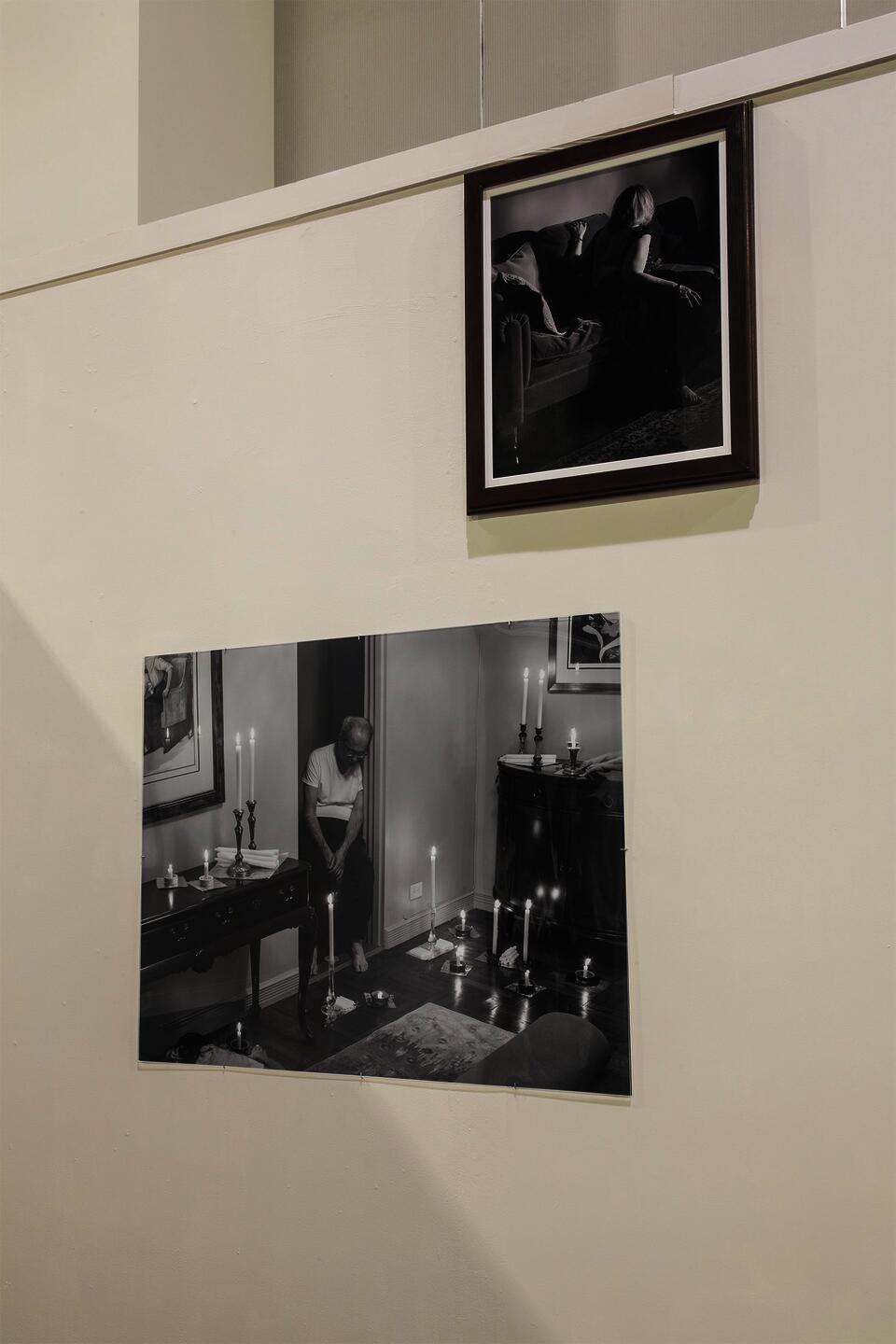Framed black and white photograph of woman on a couch with an undone dress above a photograph of a living room candle arrangement mounted behind plexiglass.