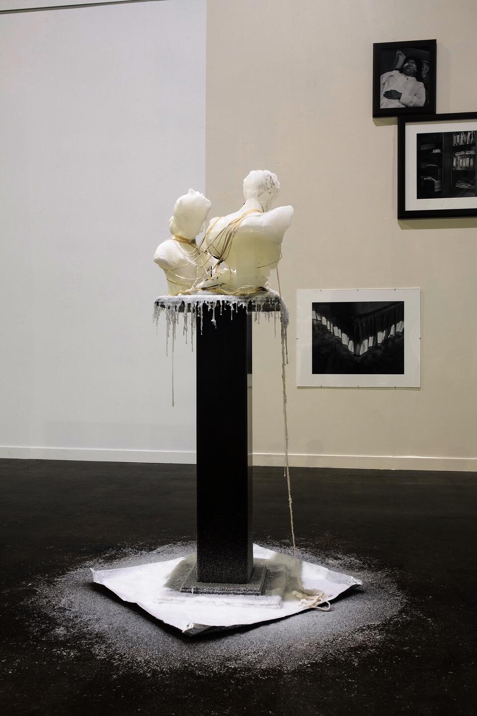 Wax sculpture on wooden podium with wax dripping from figures.