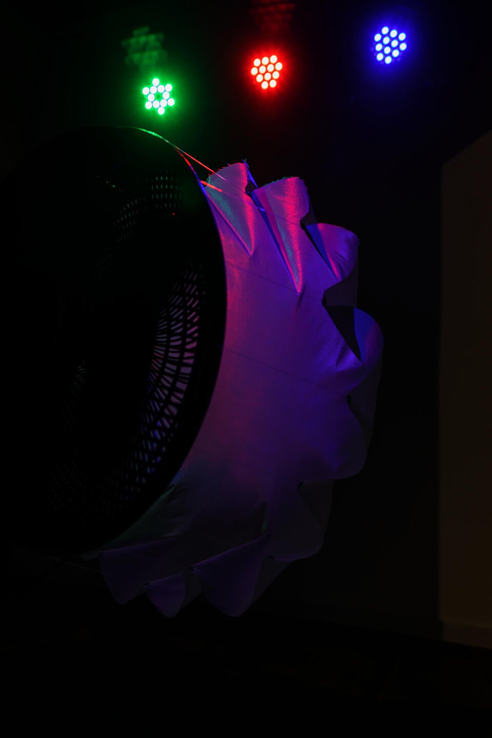 Side view of fan blowing on white fabric, with a small camera attached to the fan