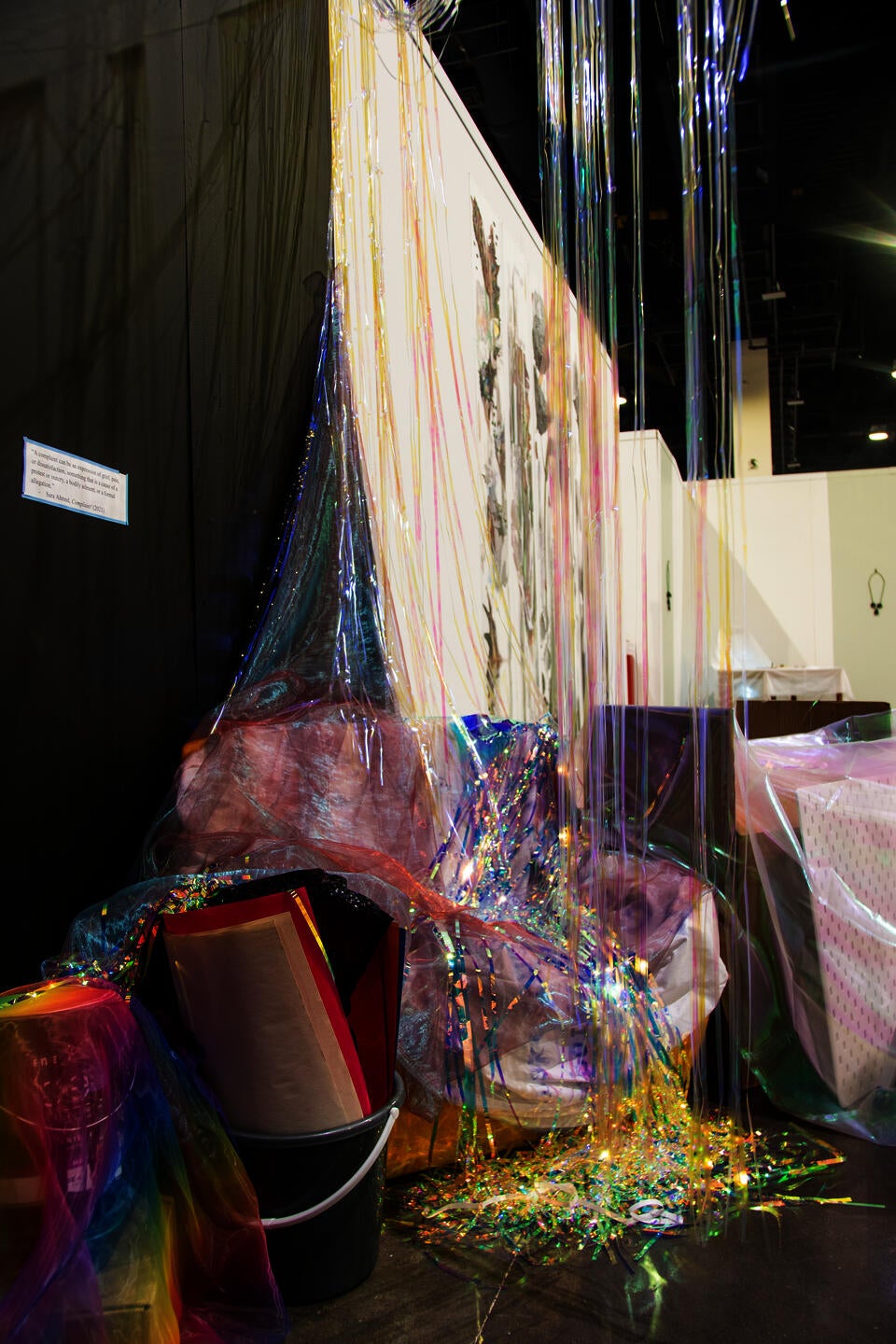 iridescent vinyl streamers hanging from above to ground; bucket filled with posters; belongings covered with fabric
