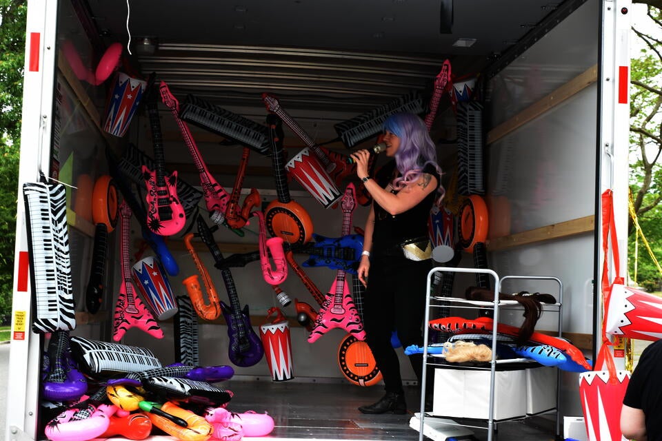 Person performing Restaurant Menu karaoke in the back of Uhaul Truck with decorated with inflatable instruments. 
