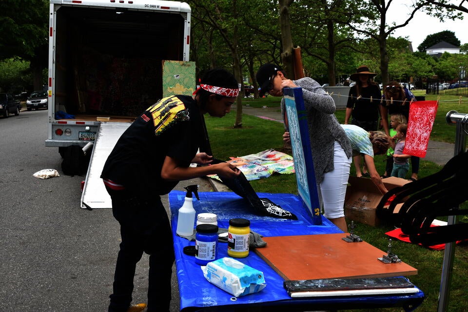 Artists screen-printing a white botanical design on black bag with the help of a participant 