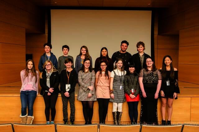 Image for sixteen young people in two rows standing in the theater with a film screen behind them. 