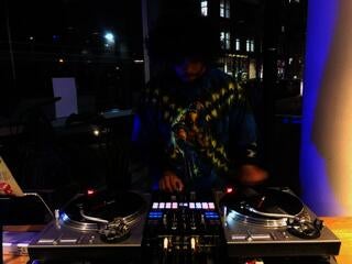 DJ in front of windows that  with the a street in the evening behind them. 