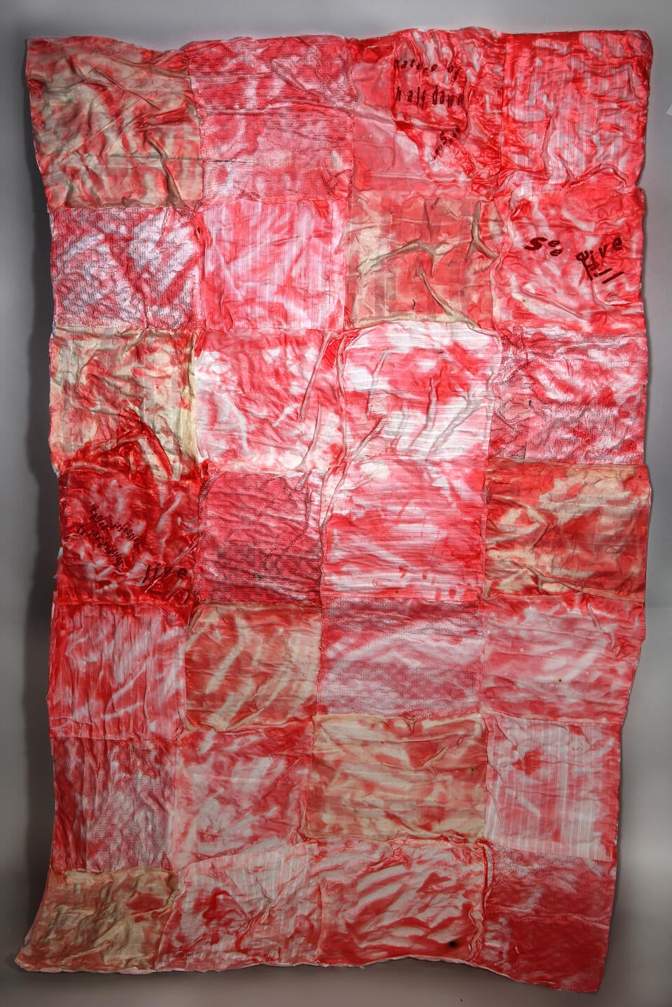 a cotton quilt with a red, plastic film and embroidered text over it reading " Nature of Half Dawn."