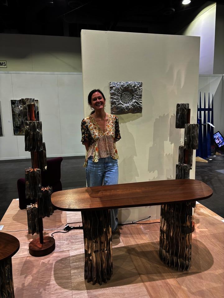 A modern furniture collection includes a coffee table, console table, pedestal table, and two floor lamps. The tables have an aluminum base and walnut tops. The floor lamps display decorative aluminum shades and central walnut stands.