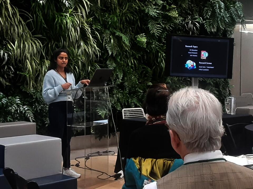 Deanne Fernandes wearing a blue sweater presenting in front of a screen