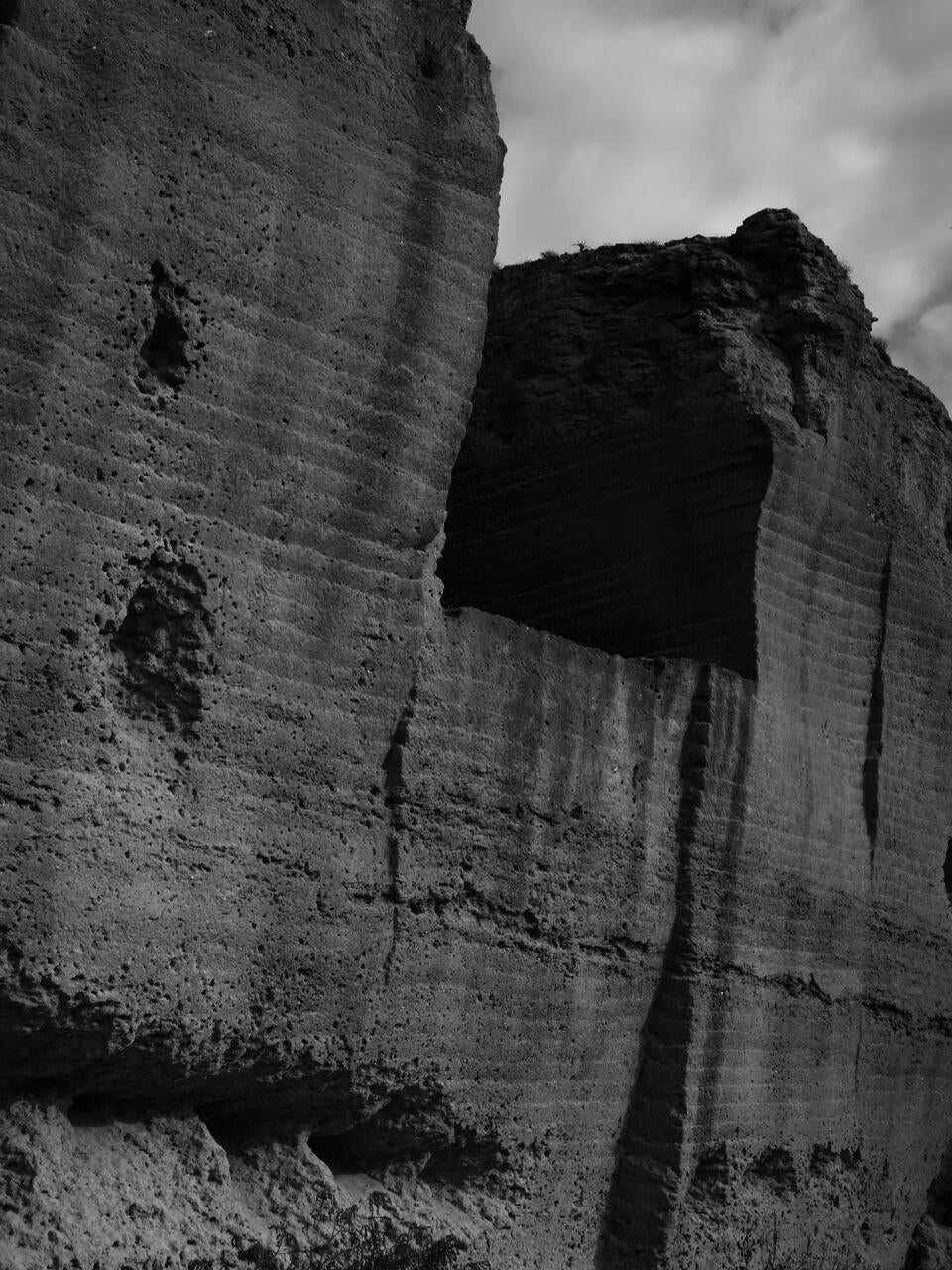 Black and white photograph of a quarry in Spain, with holes that seem erosion, but that are made because of bullets. The police used the space as a practice shooting field