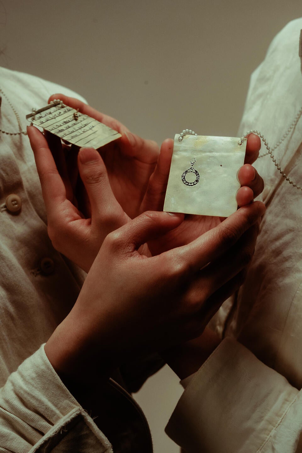 Hands holding 2 yellow pendants, one facing front and one facing back. The front is a black earring pattern with a hole, the back is written black words. Nostalgia.