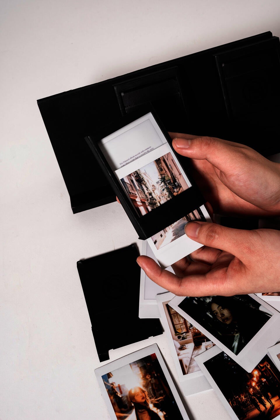 A hand pulling a Polaroid street photo from a black frame case. Polaroid photos on the background and 2 frame cases.