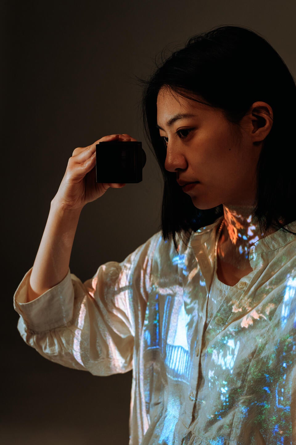 A girl is looking through a lens that has a projection inside. In one of her clothes, a corresponding image is projected.