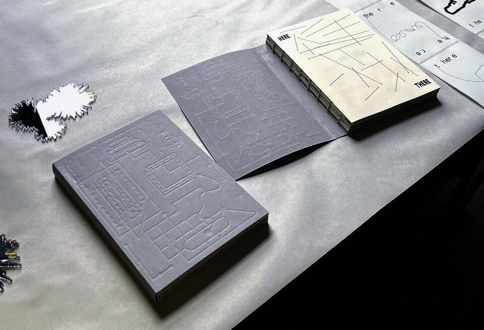 A desk with two grey books on it The cover of the book is a debossed illustration of lines and arrows.