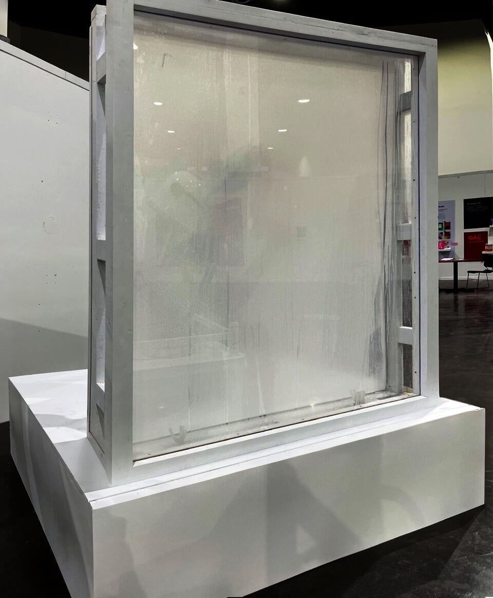 A white square stage with a window erected on one edge, with white frames and fog and condensation obscuring visibility. 