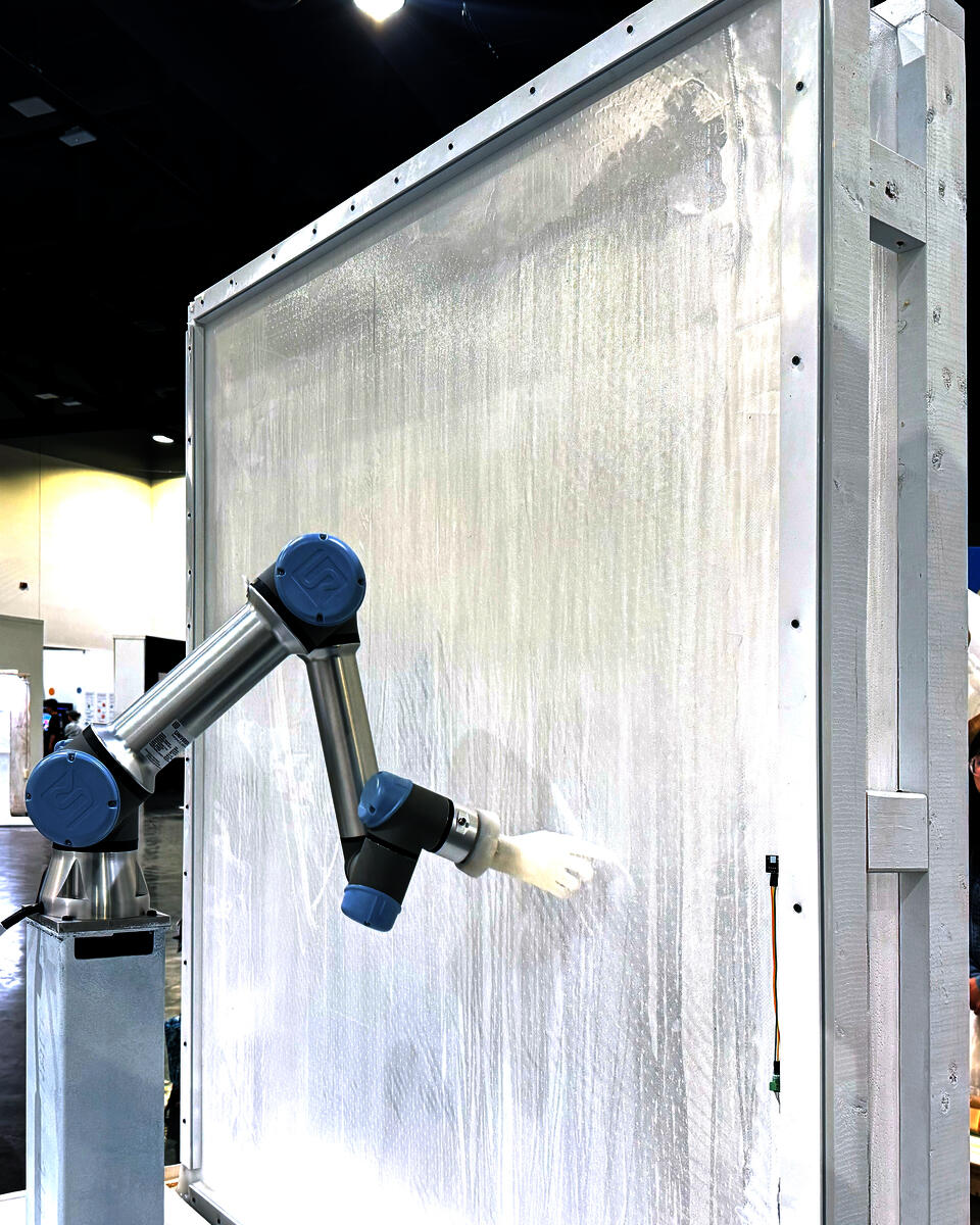 A robotic arm with white silicone hand, grazing a semi-translucent membrane with its index finger.
