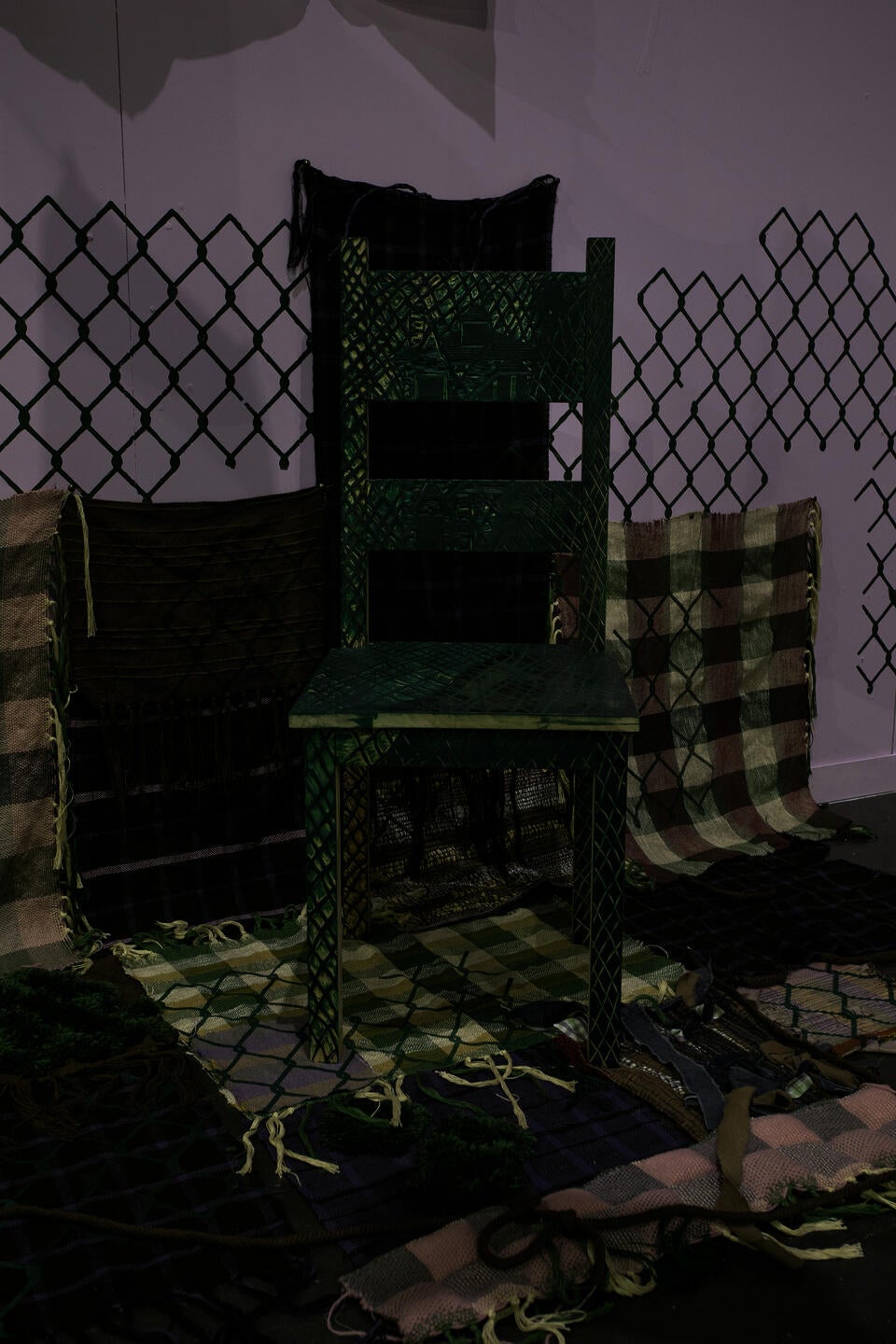image of carved green chair standing on top of woven fabrics travelling from the wall to the floor with chainlink motif printed on top with purple background