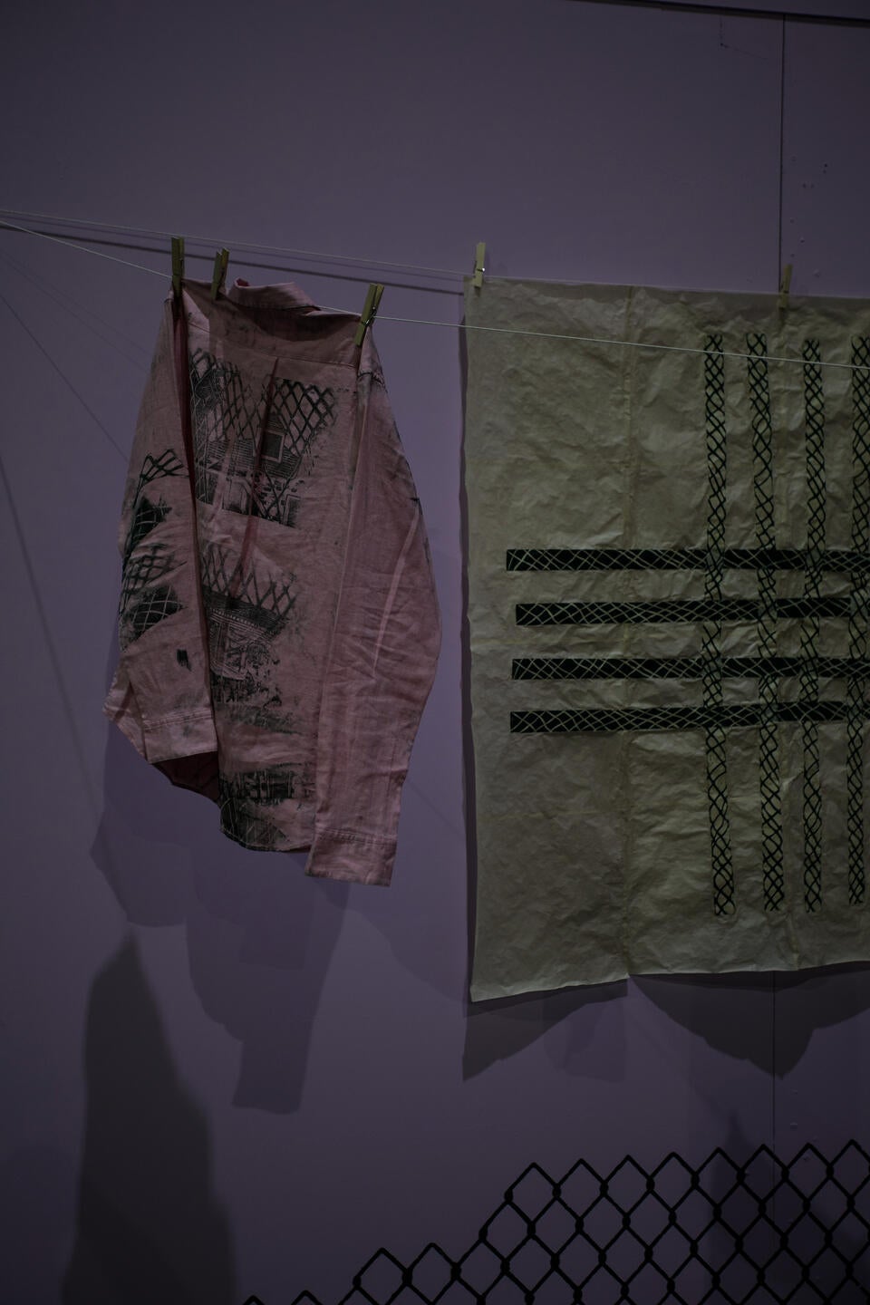 pink shirt with green woodcut prints depicting a house and intersecting lines 