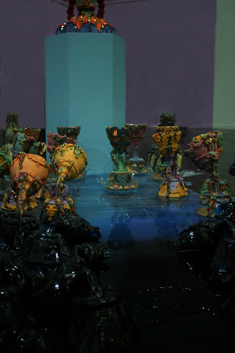 Colorful ceramic vessels arranged in clusters on a reflective surface, with a central pedestal holding an elaborate piece. The holy grails are gradually changing colors.   