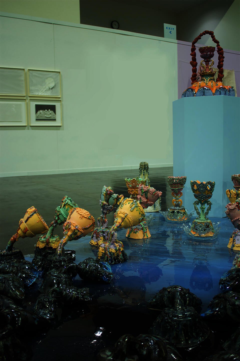 Colorful ceramic vessels arranged in clusters on a reflective surface, with a central pedestal holding an elaborate piece. The holy grails are gradually changing colors.   