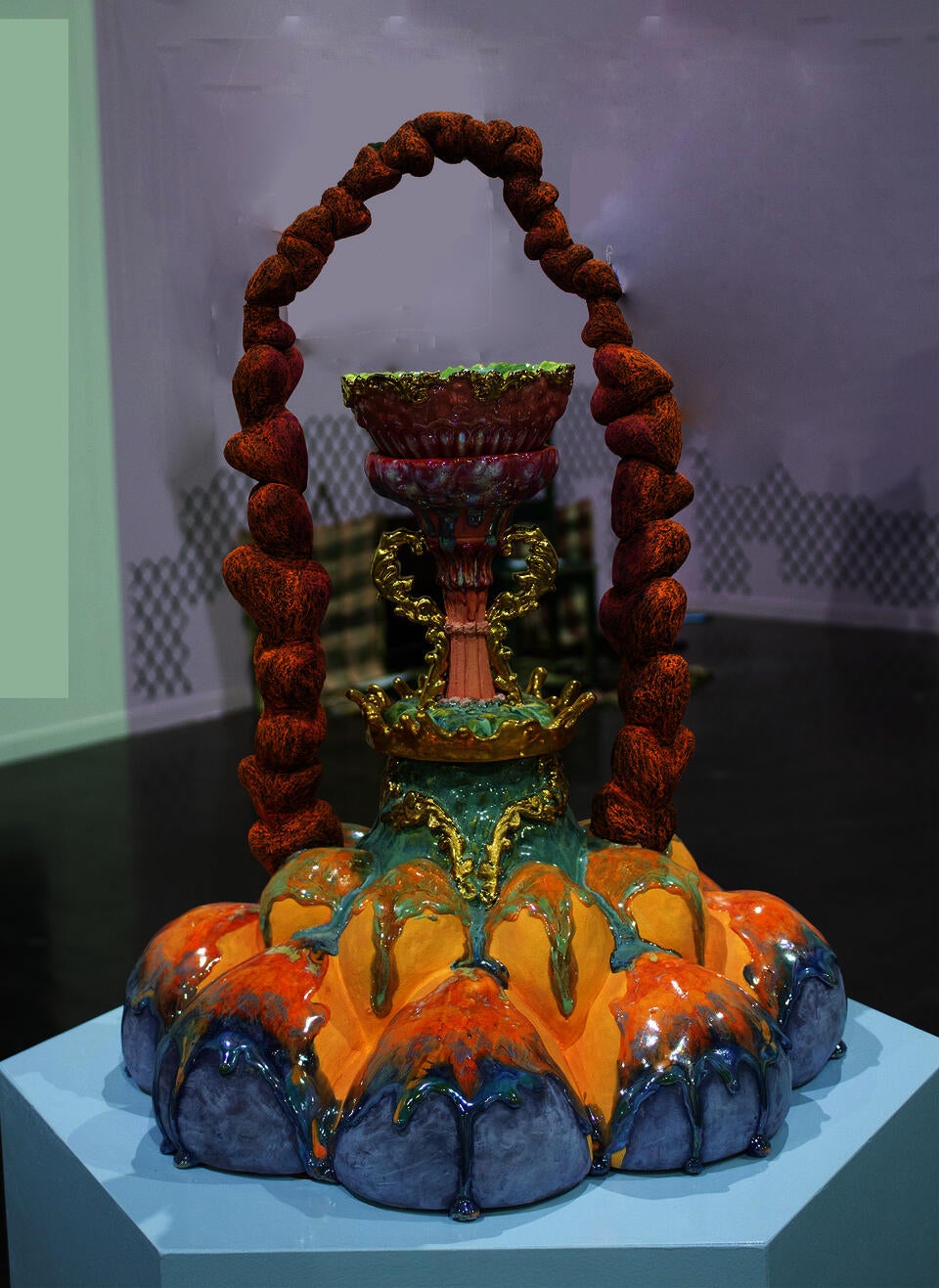 An elaborate ceramic sculpture with vibrant orange, blue, and gold hues, featuring drip-like textures and intricate details. It is an abstract form of flower. 