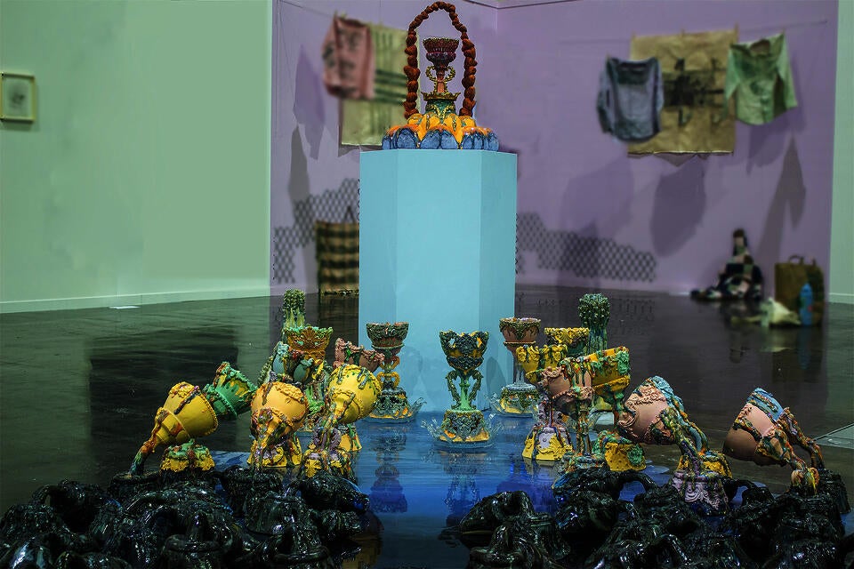 Colorful ceramic vessels arranged in clusters on a reflective surface, with a central pedestal holding an elaborate piece. The holy grails are gradually changing colors.