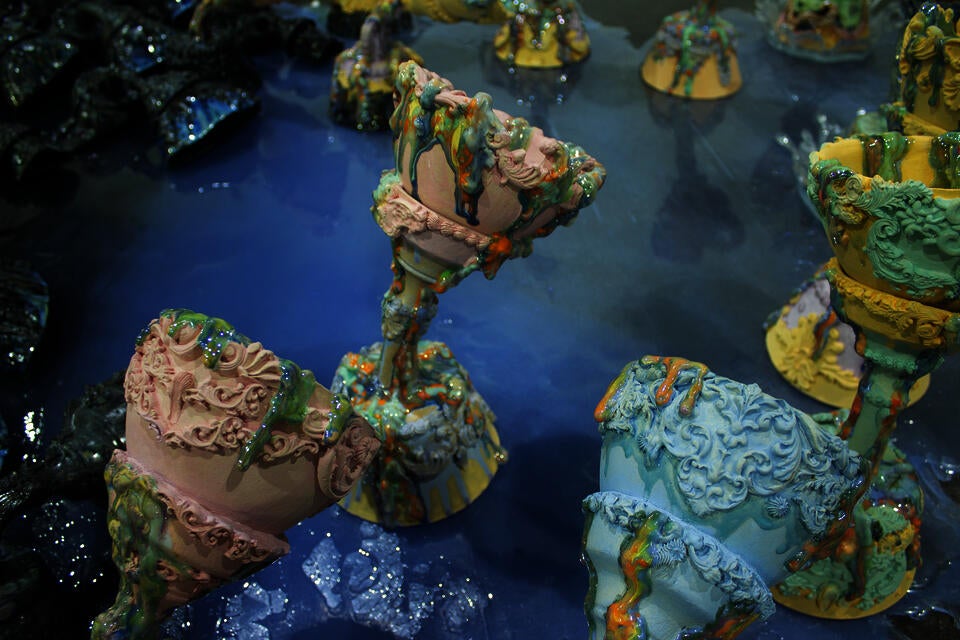 Close-up of intricately decorated the Holy grail with dripping glazed surfaces and covered with pastel colors, standing on a glossy blue reflective surface which is water.