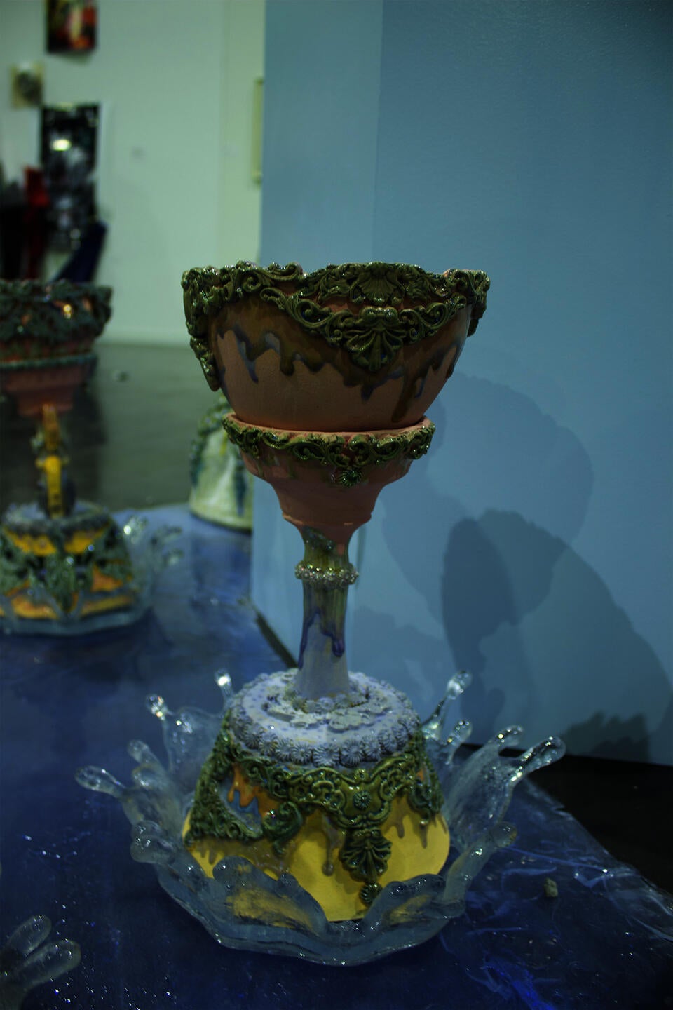 Close up of one of the Holy Grails with intricate details and pastel colors, positioned on a reflective surface. The piece has leafy patterns and a drip design.