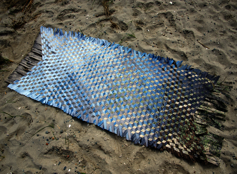 Woven photographs on paper displayed on sand.
