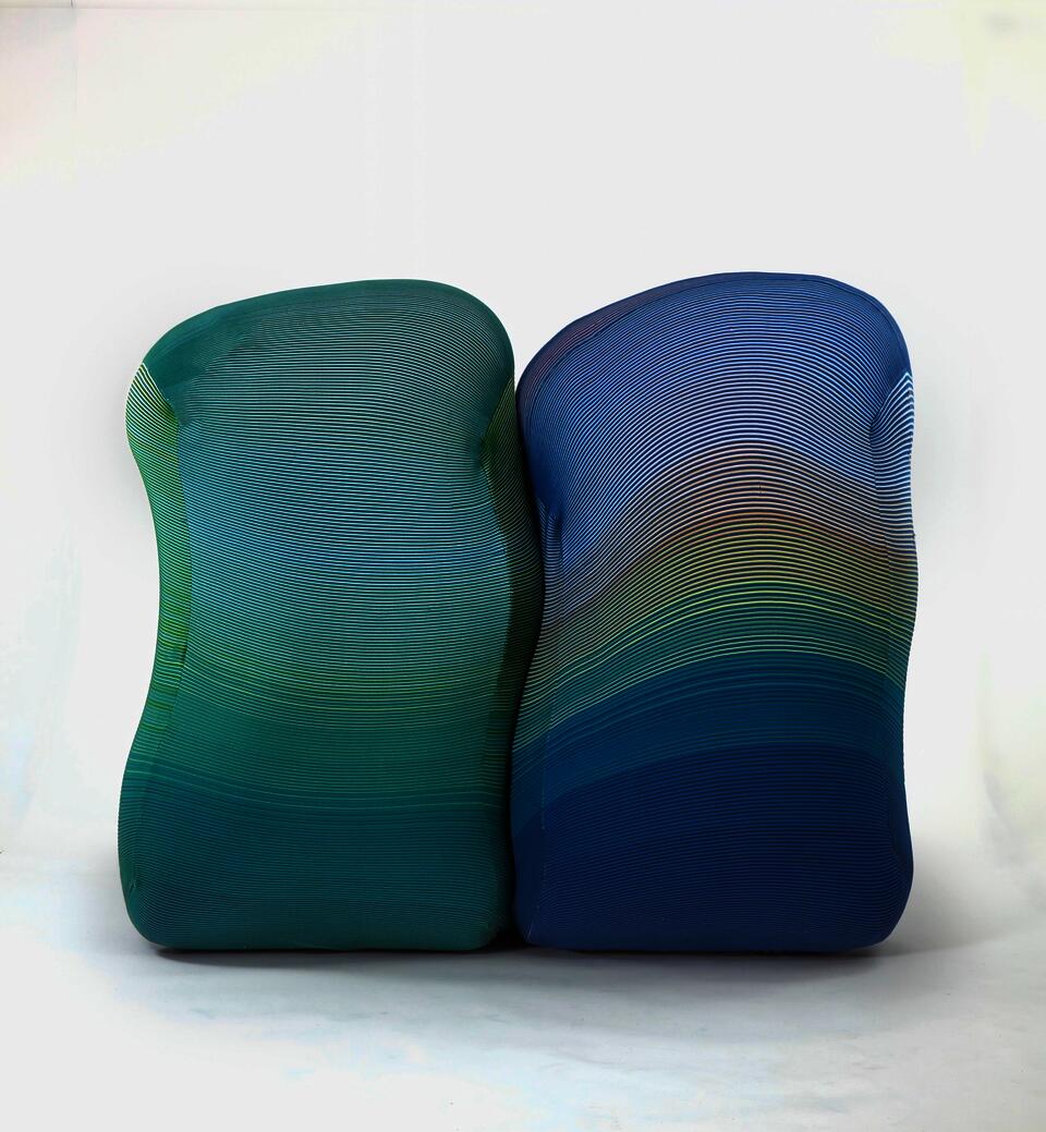 Two inflatable walls in the shape of wiggles sit side by side. They are covered in a striped knit fabric. The five foot tall walls create a division of space and an opportunity for privacy.