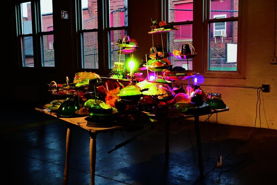 A kichen table overflowing with geletin molds that have objects imbedded in them sitting on stacked aluminum serving dishes. The entire table vibrates.