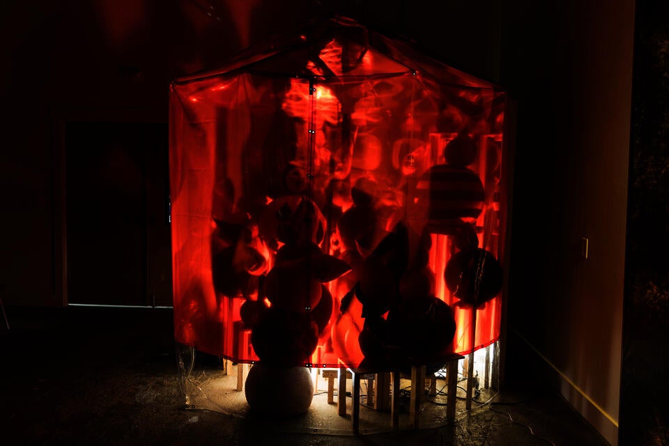 A large circus tent covered in red welding shield with somemen looking figures who slowly shake their heads back and forth.