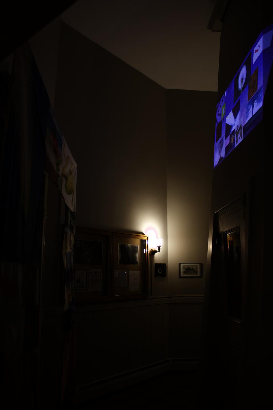 An image of a darkened interior space, a doorway covered in fabric and an animation with multiple moving windows projected on opposite wall