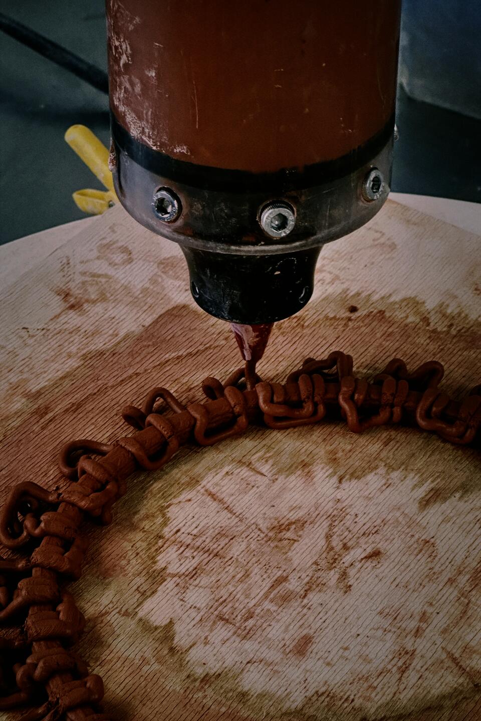 Close-up of a 3D printer nozzle extruding intricate clay patterns on a rotating wooden platform.