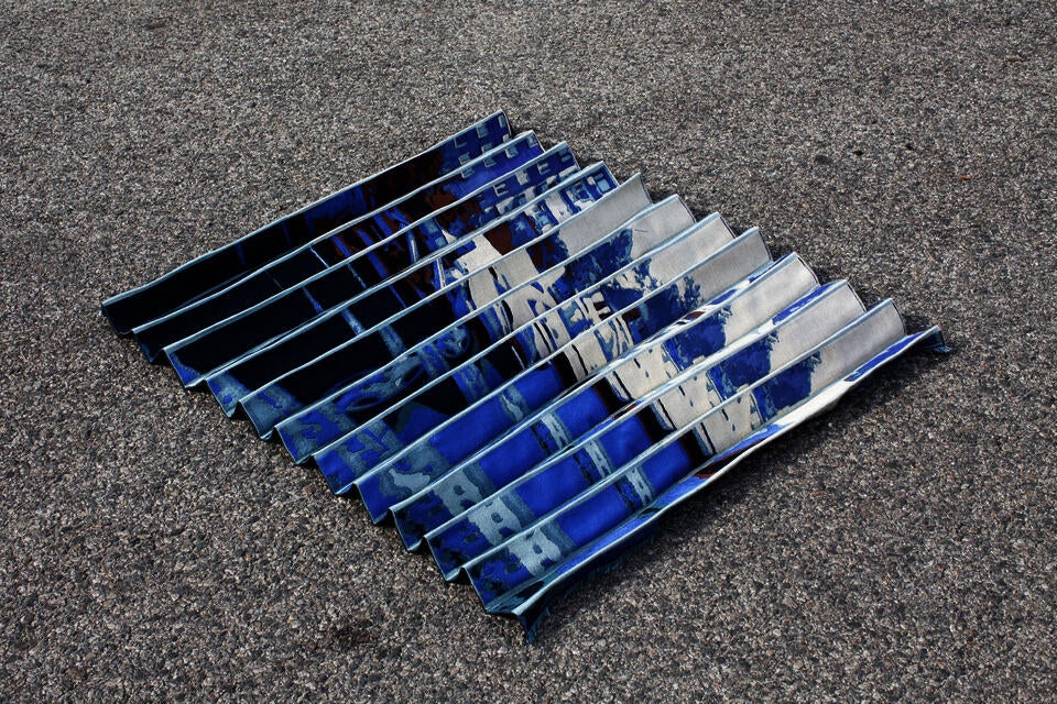 Pleated woven textile depicting a glitched image of a street in a monochromatic blue color palette.