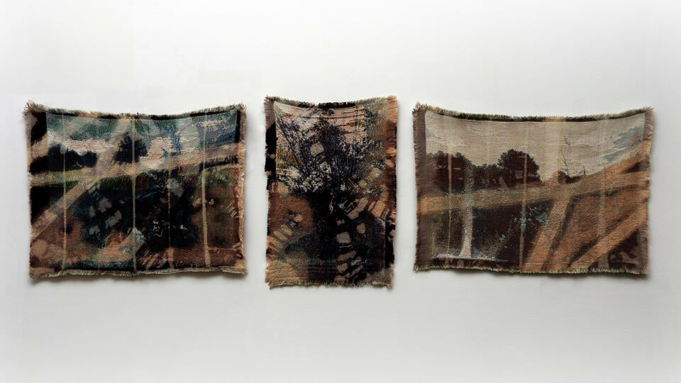 Three Small Scale weavings depicting blurry landscapes hanging in a horizontal row.