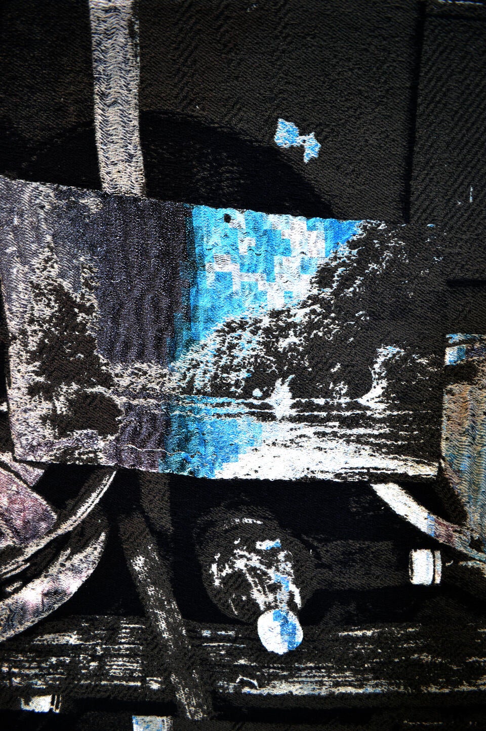 An image depicting a close up of a weaving. The close up shows one repeat of a larger work with a landscape and a plastic bottle in a greyscale color palette.