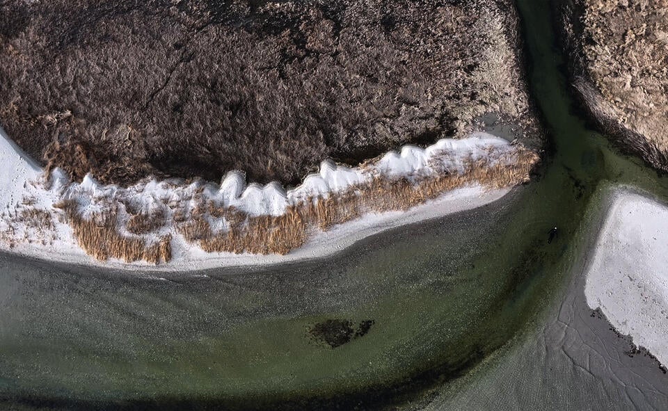 Drone footage of a person floating in the mouth of a salt marsh channel.