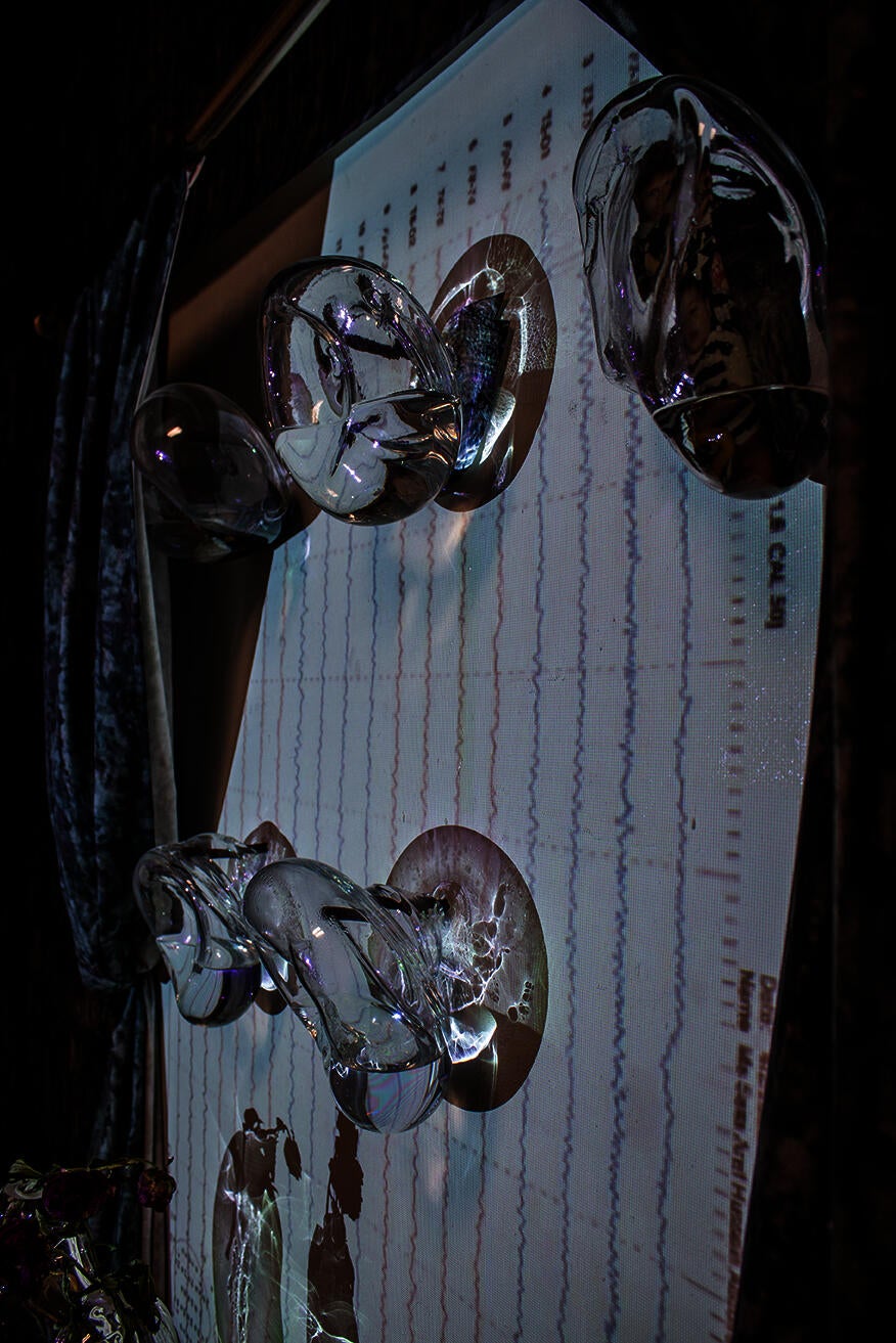 Close-up detail of an intriguing installation. Glass orbs capture the impression of limbs from a casted body, delicately holding liquid and childhood photographs within them. 