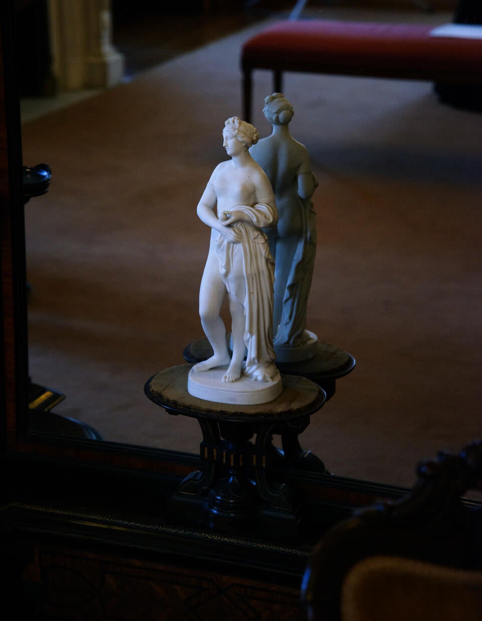 A marble statue of the Greco-roman goddess, Venus, posed against a mirrored background. Reflected in the mirror is the carpet of an interior room.  