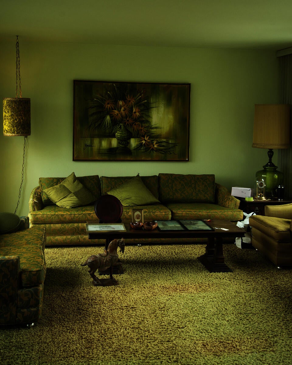 An monochromatic (olive green) interior space of a mid-century modern living room paired with matching furniture. On the floor is a sculpture of a horse figurine and a coffee table. 