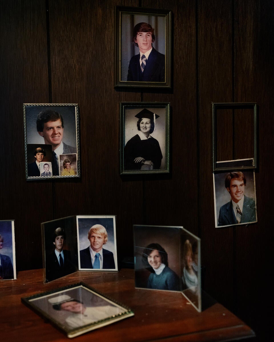 Framed photographs mounted on a wood-paneled wall of men and women in various portraits. A sidetable below features additional photographs.